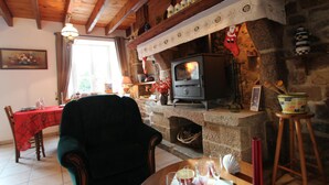 Un salon chaleureux avec une cheminée en pierre, un plafond en bois et un coin repas agrémenté d’une nappe rouge.
