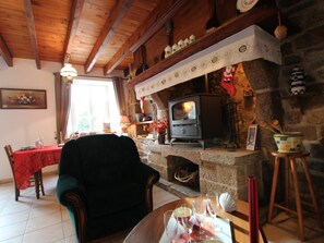 A cozy living room with a stone fireplace, a wooden ceiling, and a dining area with a red tablecloth.