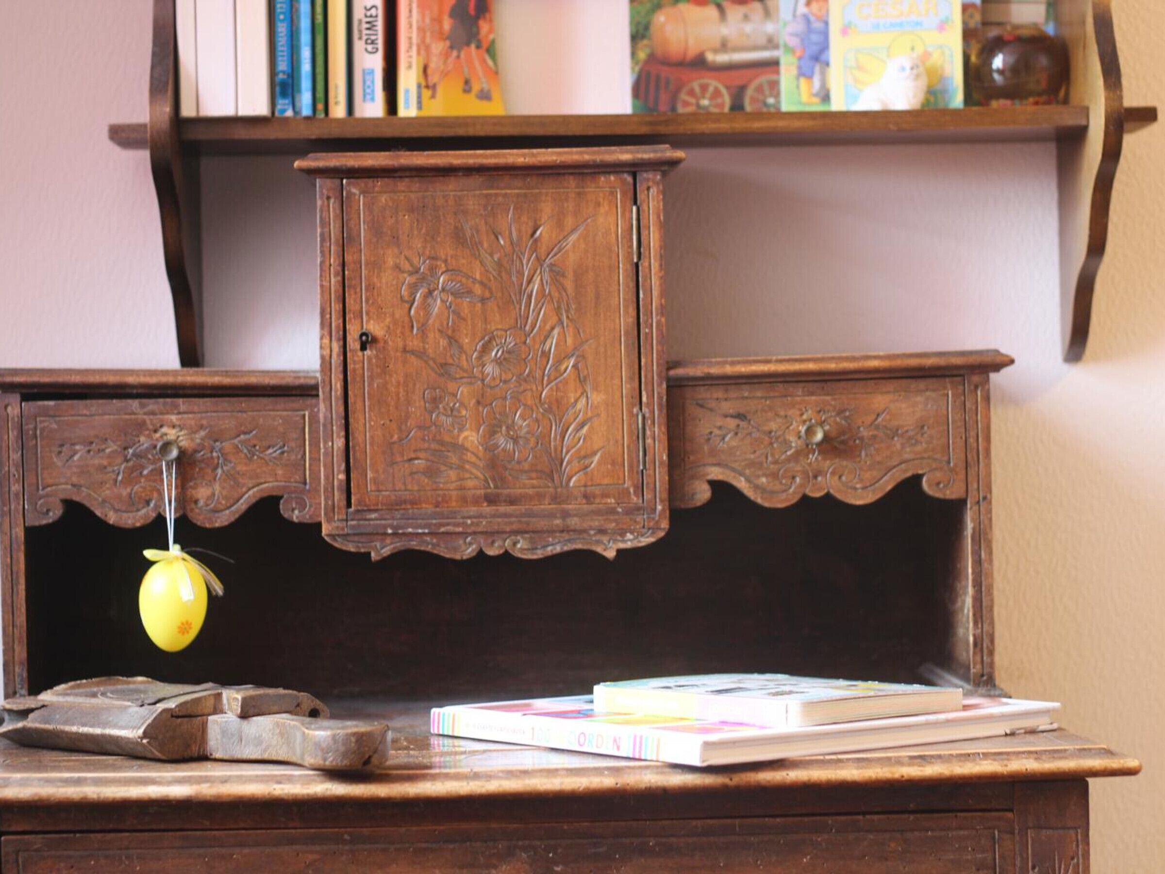 Un bureau en bois avec un petit meuble de rangement, un œuf jaune et des livres.
