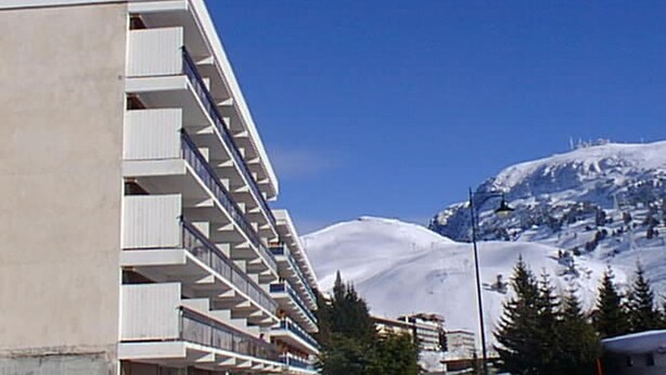 Un hôtel à plusieurs étages doté de balcons, une montagne enneigée en arrière-plan et un ciel bleu dégagé.