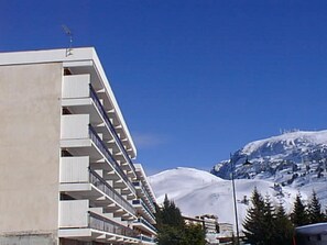 Een meerhoog hotel met balkons, een met sneeuw bedekte berg op de achtergrond en een helderblauwe lucht.