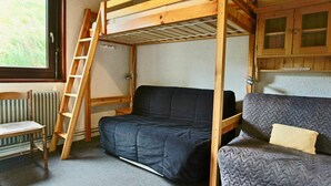 Une petite pièce comprenant un lit superposé, un canapé, une chaise et une fenêtre.