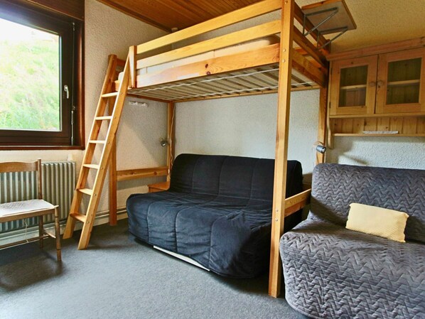 Een kleine kamer met een stapelbed, een slaapbank, een stoel en een raam.