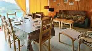 Un coin repas avec une table dressée pour quatre personnes, des chaises en bois, un canapé et un téléviseur fixé à un mur en bois.