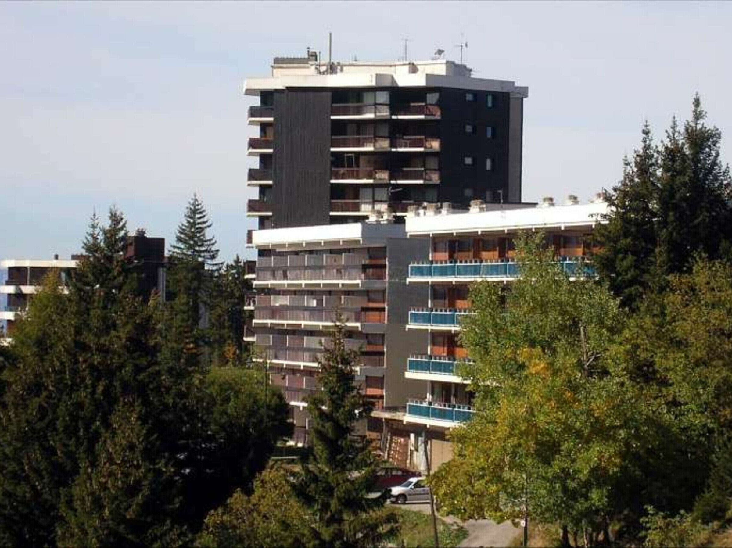 A multi-story building with balconies, surrounded by trees.