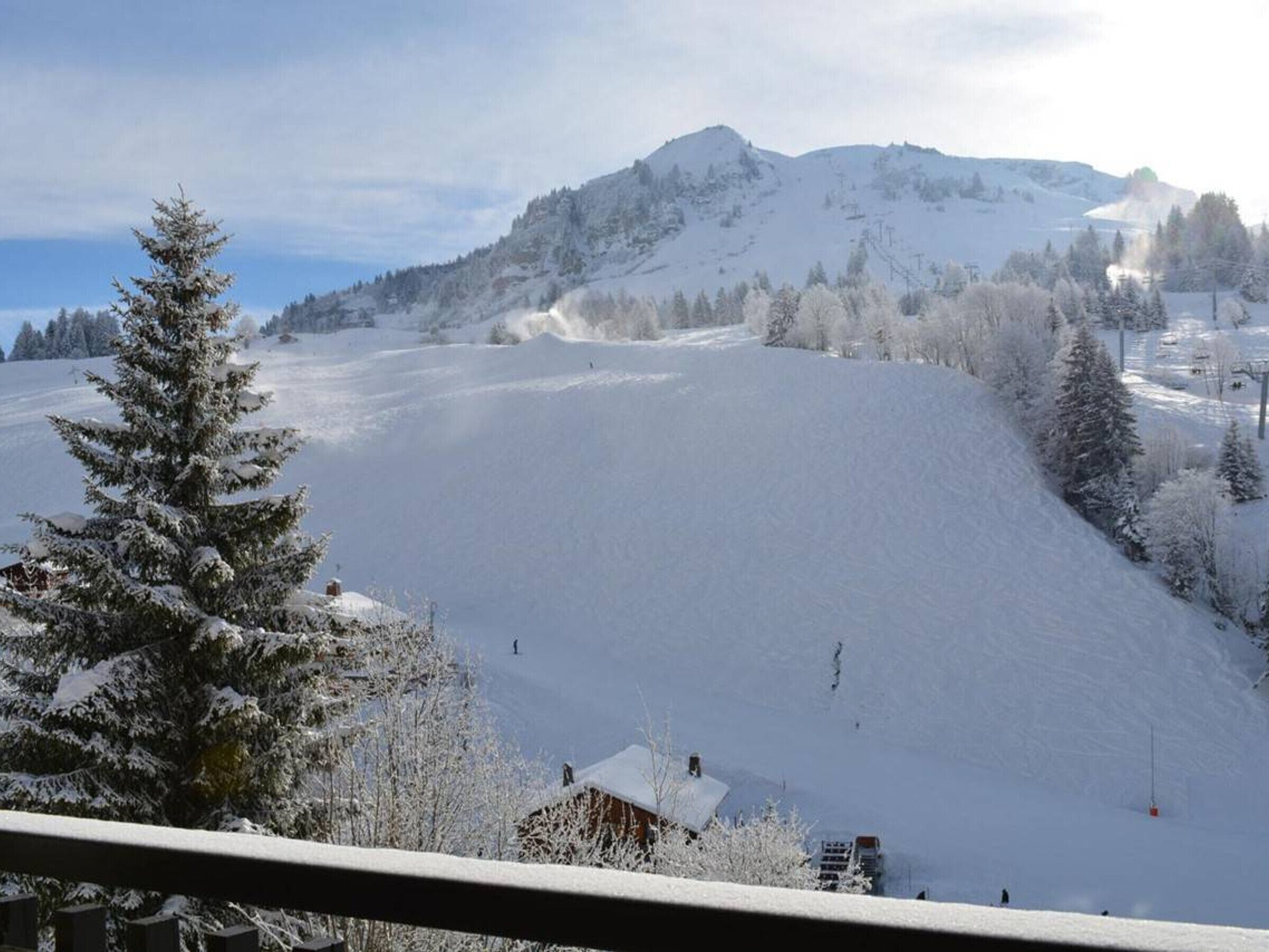 A snow-covered mountain landscape with a ski slope, trees, and a building in the foreground.