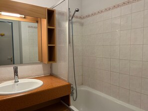 A bathroom with a white sink, a wooden vanity, a mirror, a shower, and tiled walls.