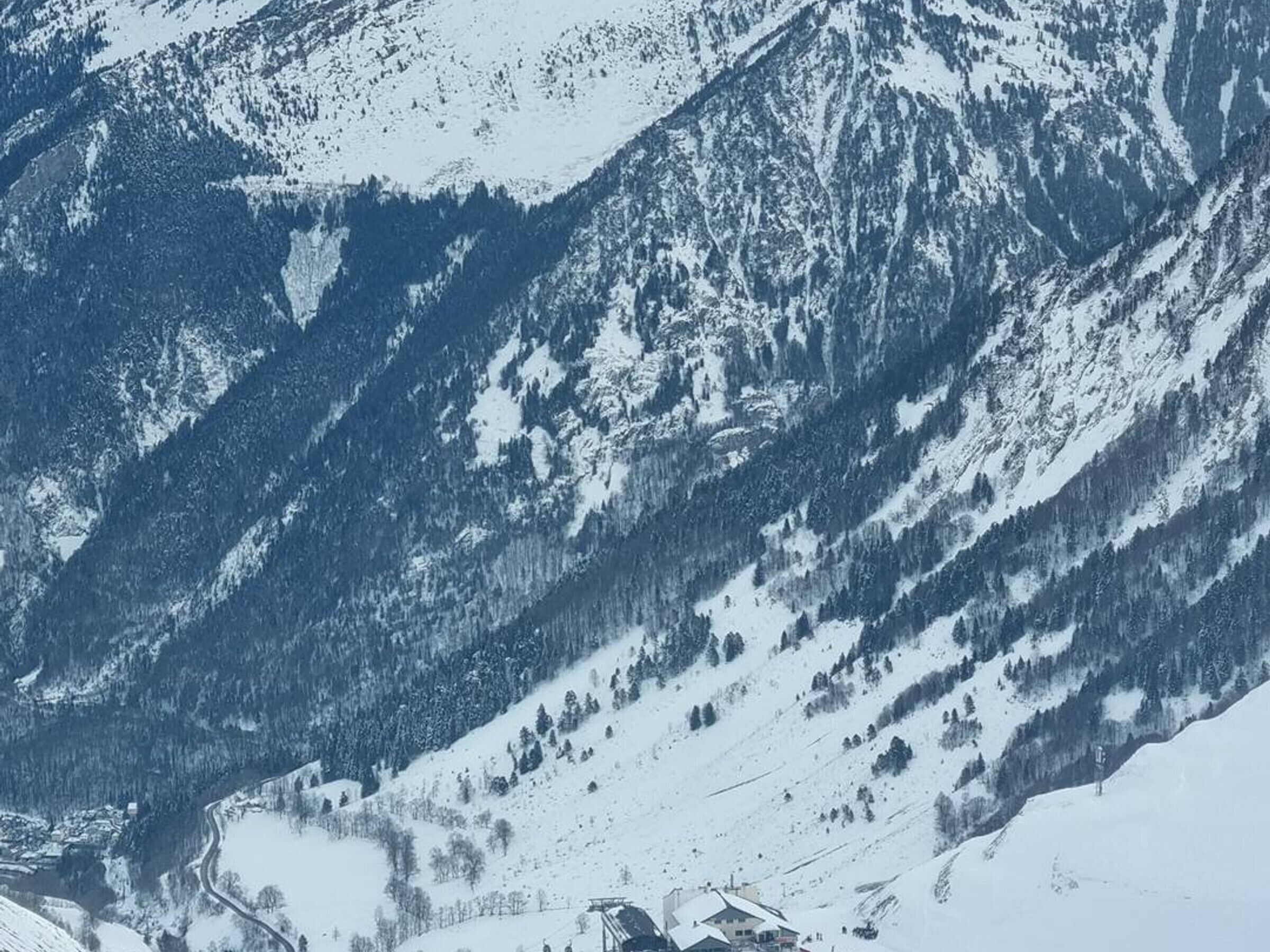 Un paysage montagneux aux pentes enneigées, avec un petit bâtiment situé au pied de la montagne.