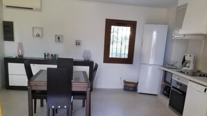 Een kleine keuken met een koelkast, fornuis en gootsteen. Er is een zithoek met een tafel en stoelen.