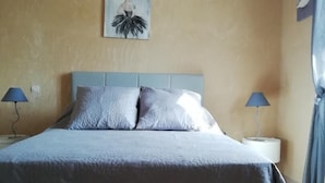 Een slaapkamer met een bed, twee bedlampen, een kunstwerk aan de muur en een gordijn.