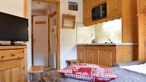 Una habitación compacta con cama, televisión, kitchenette con armarios de madera y una pequeña mesa.