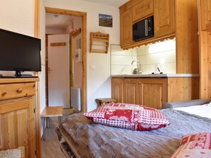 Una habitación compacta con cama, televisión, kitchenette con armarios de madera y una pequeña mesa.