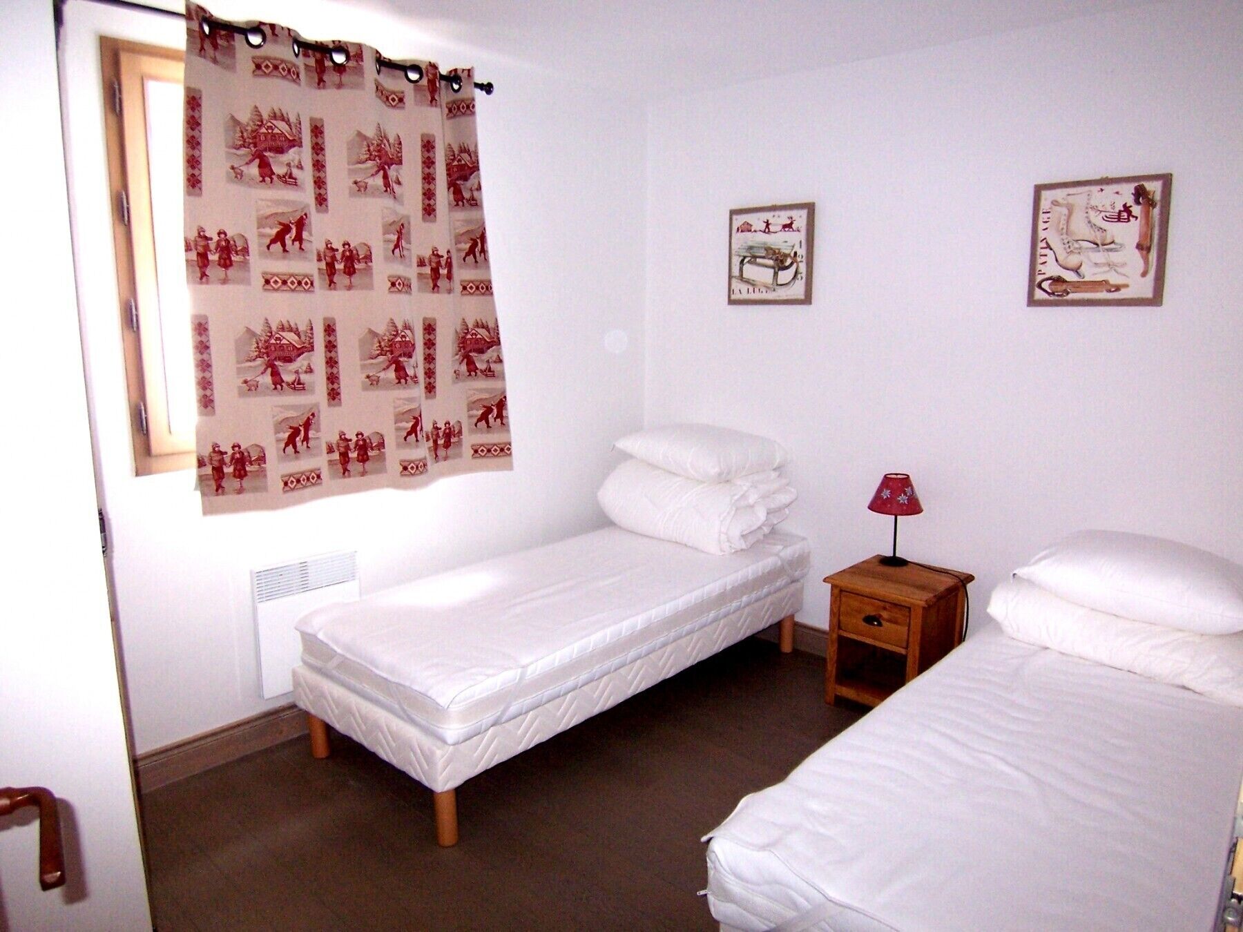 A bedroom with two single beds, a wooden nightstand with a lamp, and a window with a curtain.