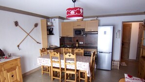 A compact kitchen with a refrigerator, microwave, and stove. There is a dining table with chairs and a small sofa. - D002 - 60 m2 - 3P+cab - 6/8 pers (Prapoutel)