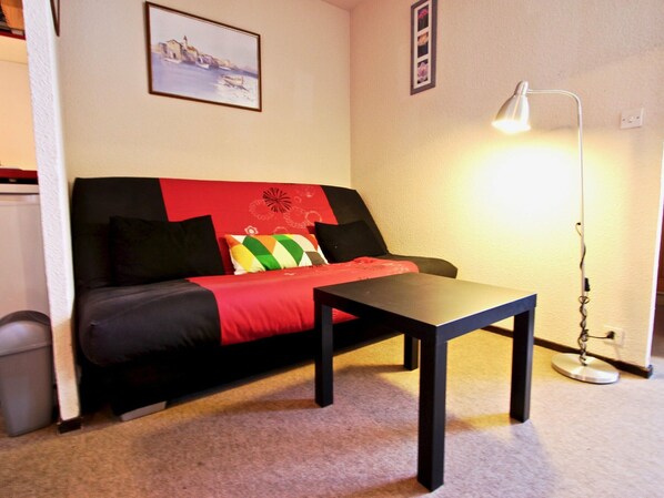 A small, cozy room with a red and black sofa, a small table, and a floor lamp.
