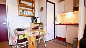 Pieni, käytännöllinen keittiö, jossa on puinen pöytä, valkoiset tuolit ja jääkaappi.