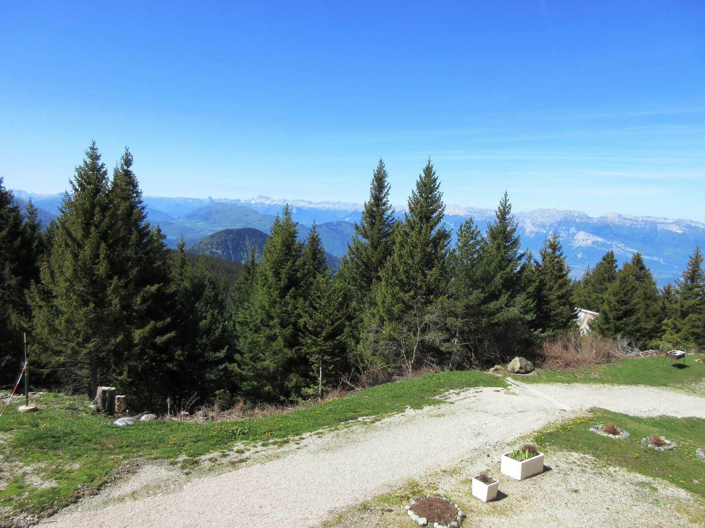 Un paysage montagneux, avec une végétation dense de conifères, un sentier de gravier et un ciel bleu clair.