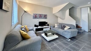 Un salon moderne avec deux canapés gris, une table basse en verre, un téléviseur à écran plat et des œuvres d’art abstraites accrochées au mur.