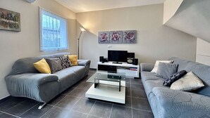 Un salon moderne avec deux canapés gris, une table basse en verre, un téléviseur à écran plat et des œuvres d’art accrochées au mur.
