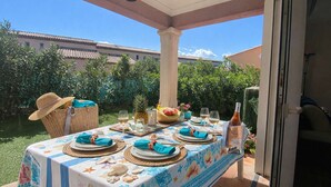 Un espace de restauration en plein air avec une table dressée pour quatre personnes, agrémenté d’une nappe aux motifs tropicaux, de paniers en osier et d’une bouteille de vin.