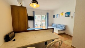 A small, cozy room with a dining table and chairs, a sofa with checkered cushions, and a view of the outside balcony. - Apartment Studio located 50m from the beach of Canyelles Petites, Roses (Rosas / Roses)