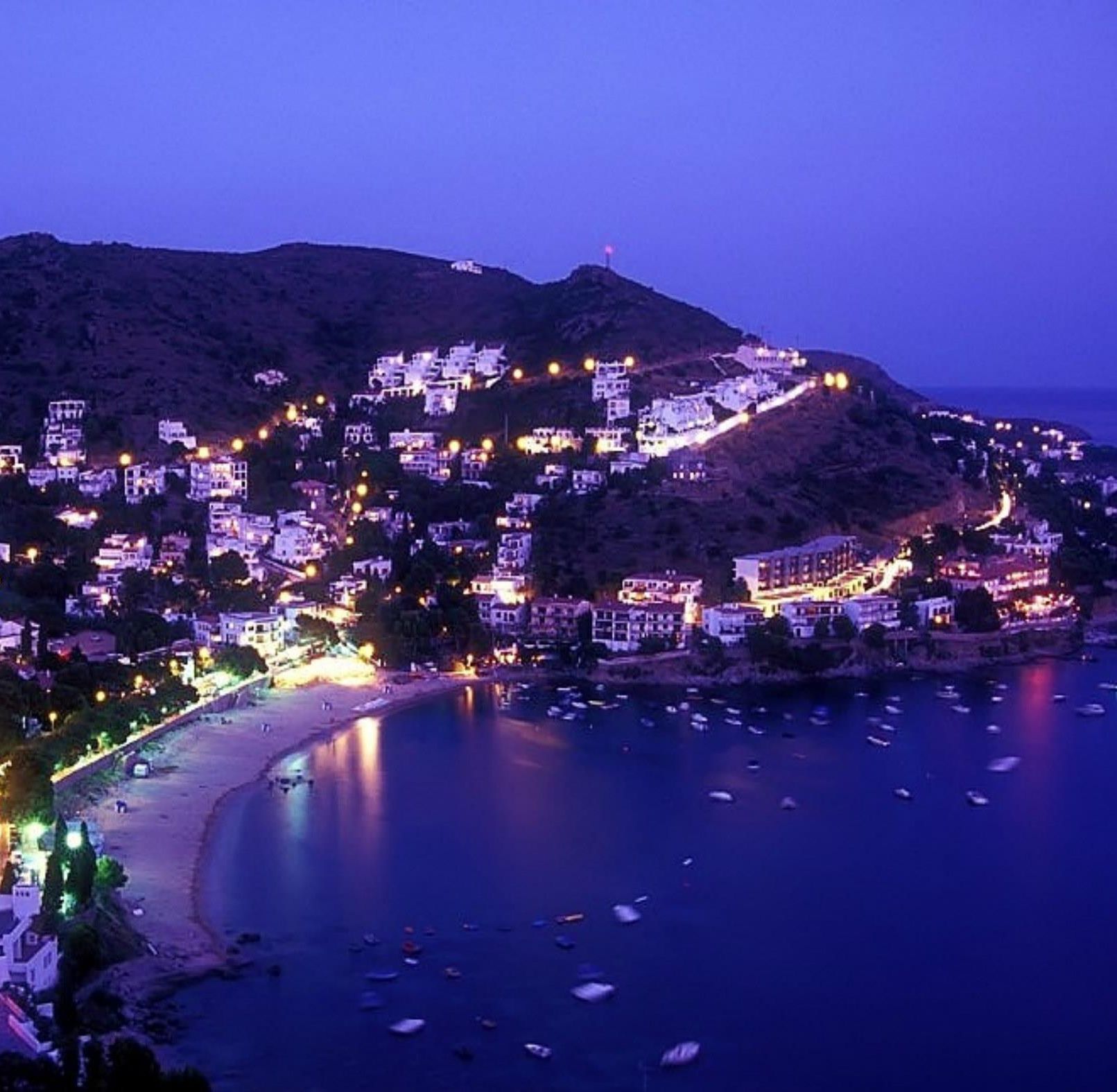 Une ville côtière au crépuscule, avec des bâtiments illuminés et une plage.