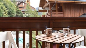A wooden deck with a table and chairs, overlooking a pool and a mountainous landscape.