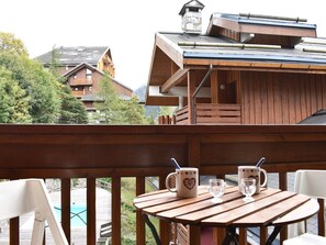 Terraza de madera con mesa y sillas, con vistas a una piscina y un paisaje montañoso.