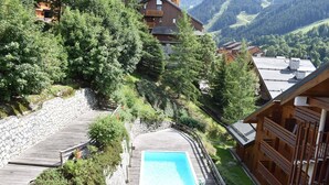 A wooden deck with a pool, surrounded by greenery and mountain views.