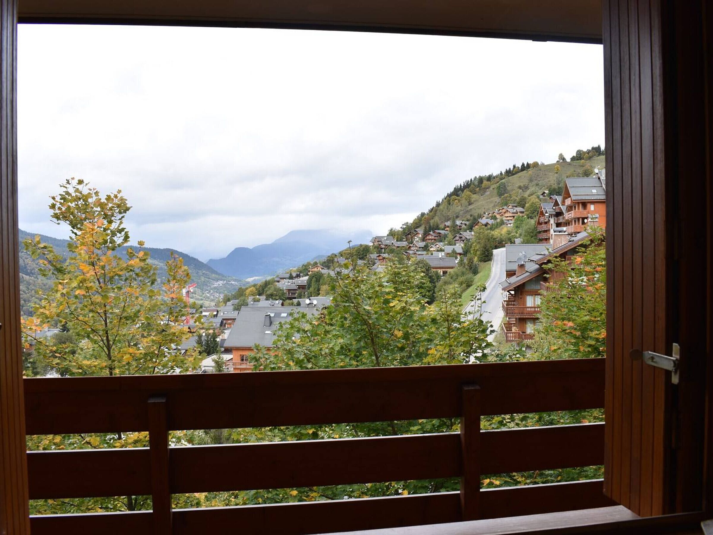 A view from a balcony with a wooden railing, overlooking a hillside with traditional wooden houses and a mountain in the background.