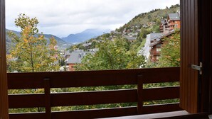 A view from a balcony with a wooden railing, overlooking a hillside with traditional wooden houses and a mountain in the background.