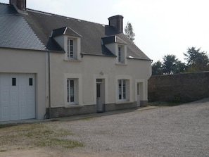A two-story building with a garage, a small porch, and a gravel driveway.