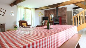 A cozy living room with a checkered tablecloth, a fireplace, and a wooden staircase. - Charming house 3 bdrms., garden, 6 pers. (Le Grand-Celland)
