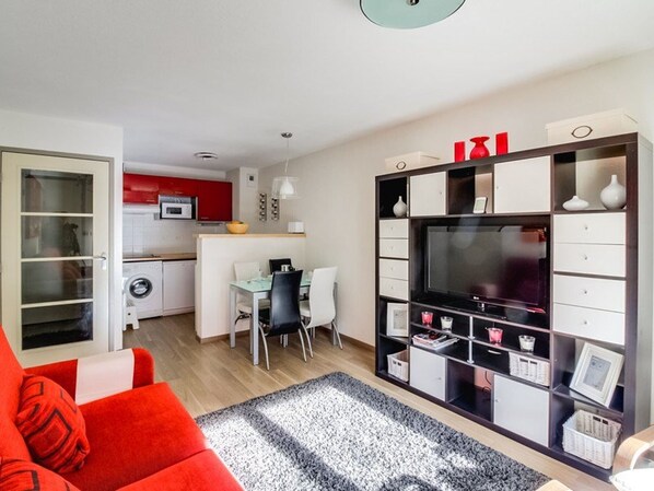 A modern living room with a red sofa, a black and white rug, and a TV stand with shelves.