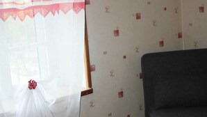 Ein Zimmer mit einem Bett, einem Fenster mit leichtem Vorhang, einem gerahmten Bild an der Wand und Wandtapete mit Muster.