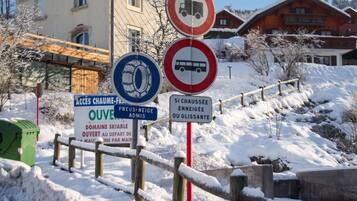 Une scène hivernale en plein air, avec une clôture en bois, une poubelle verte et plusieurs panneaux de signalisation.