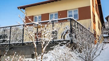 Un bâtiment à deux étages doté d’un balcon, des branches recouvertes de neige et un ciel dégagé.
