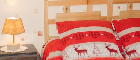 Makuuhuoneessa on puinen sänky, yöpöytä, jossa on lamppu, ja seinä, jossa on kuvioitu tapetti.