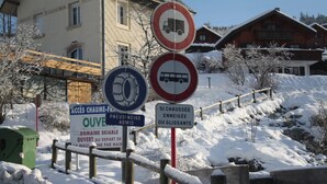Schneebedecktes Gebiet mit Schildern, die das Befahren durch Lastwagen oder Busse verbieten, und einem Schild für den Zugang zum Skigebiet.