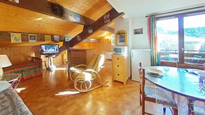 L’intérieur chaleureux d’un chalet avec un plafond en bois, un téléviseur, un fauteuil à bascule, une table à manger et un réfrigérateur.