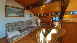 Une pièce confortable avec un canapé, un fauteuil, une télévision et un plafond en bois.