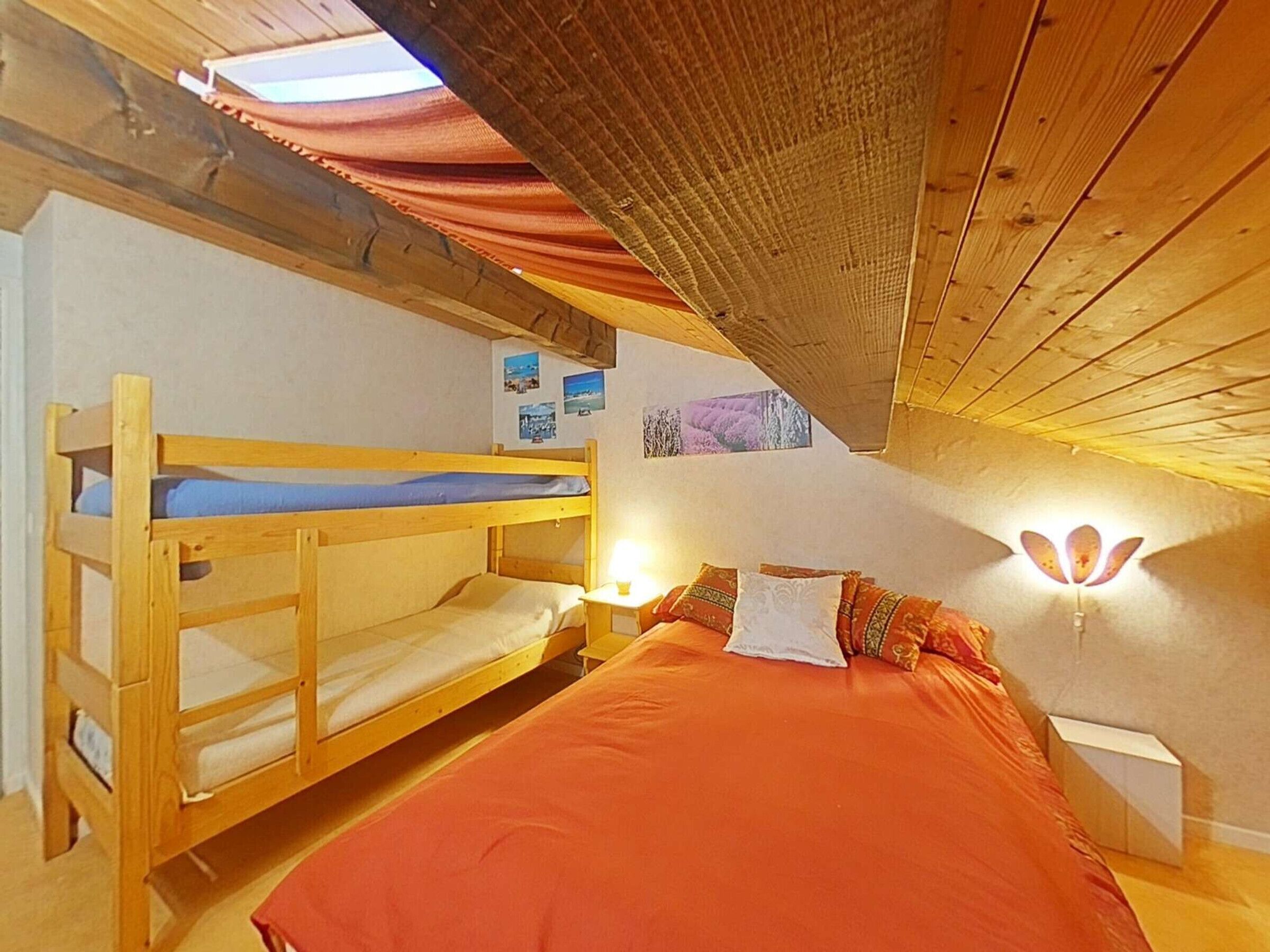 Un dormitorio con literas, una cama con colcha naranja, una mesita de noche, lámparas de pared y cuadros en la pared.