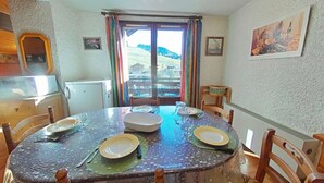 Un coin repas avec une table ronde, des chaises et une vue sur un paysage montagneux, visible à travers une grande fenêtre.