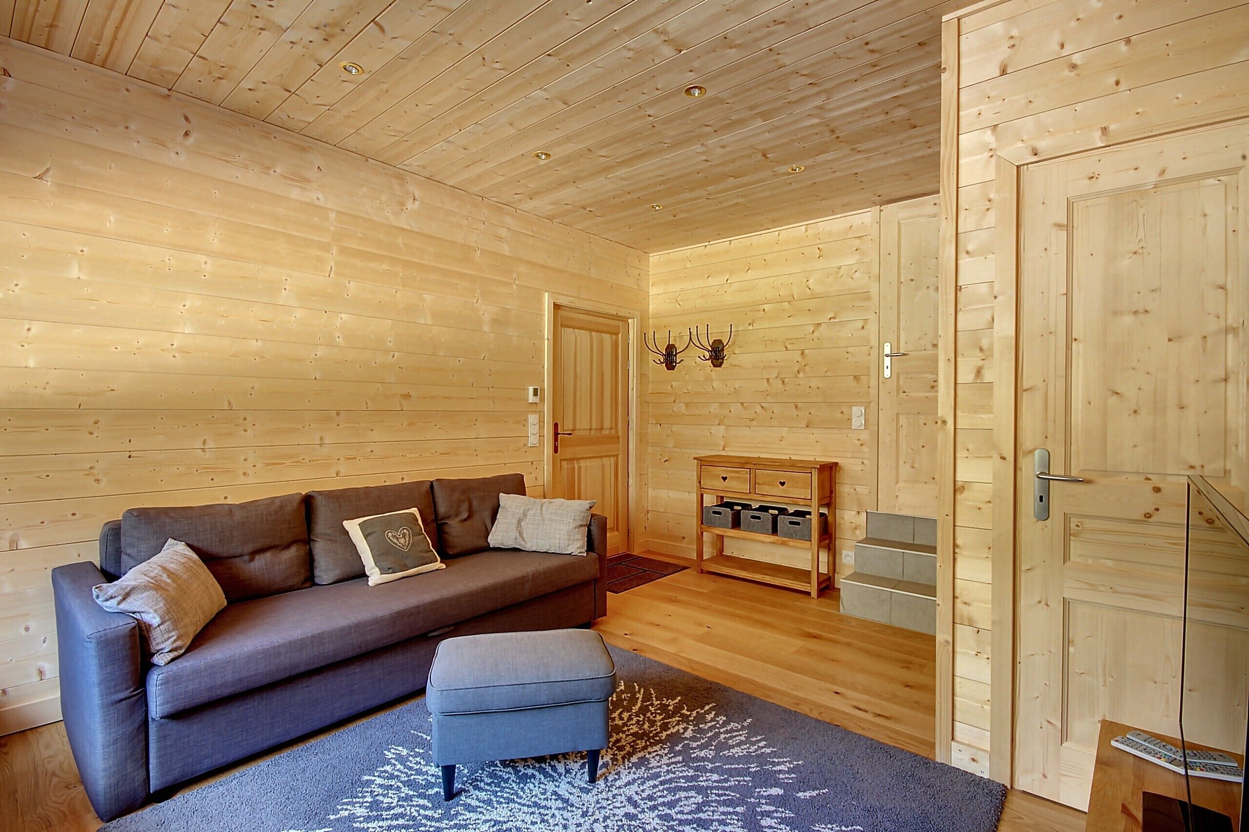 Interior de una cabaña de troncos con un sofá, un reposapiés y un aparador de madera.