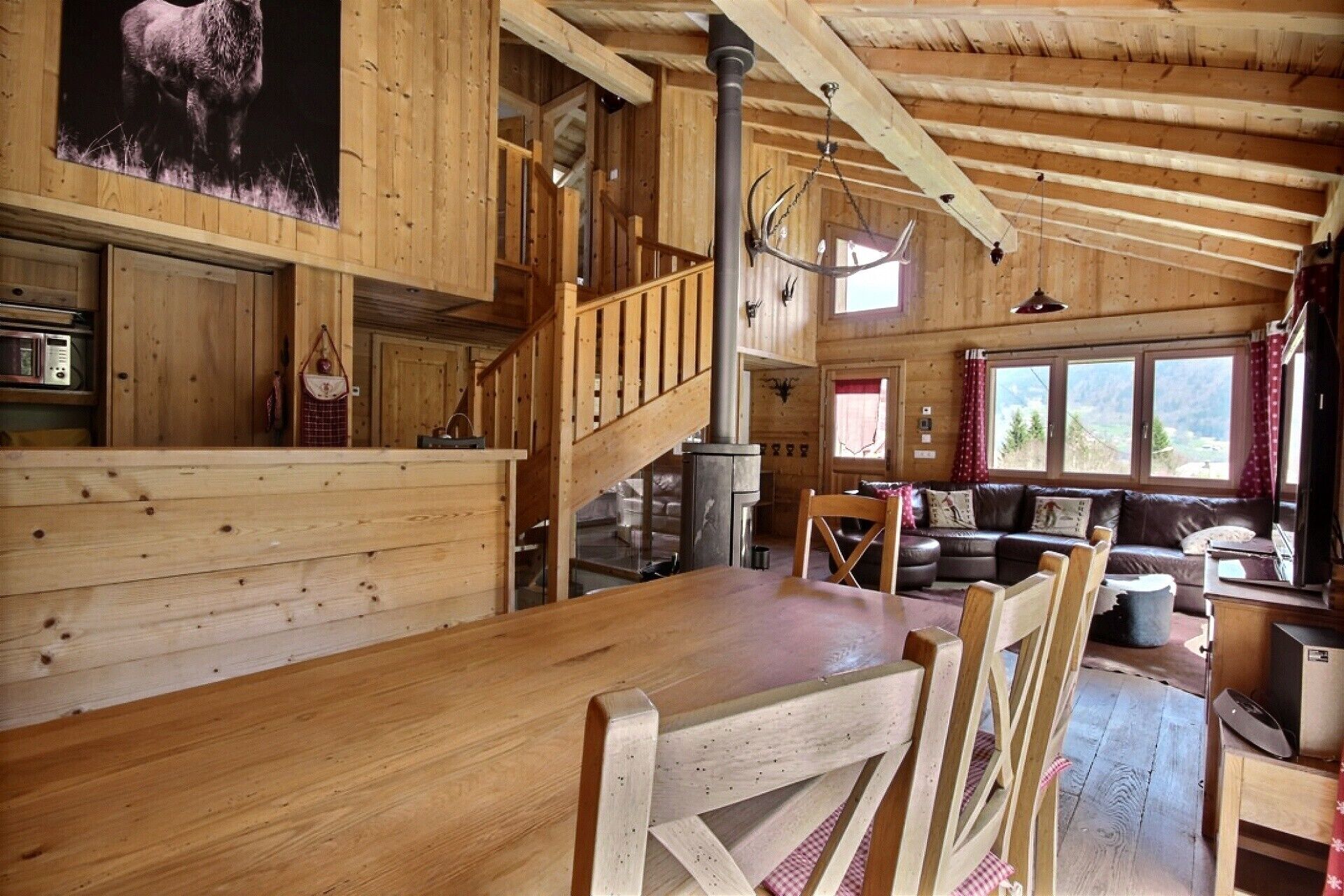 A wooden cabin interior with a dining area, a staircase, a living room with a sofa, and a fireplace.