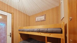 Ein Stockbett mit grauer Matratze und Holzrahmen, eine Tür mit Griff und ein gerahmtes Bild an der Wand.