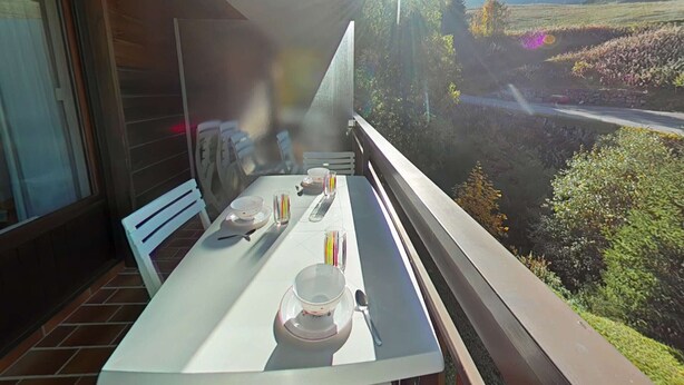 Ein Balkon mit Tisch für zwei Personen, mit Blick auf eine malerische Landschaft aus Bergen und Feldern.