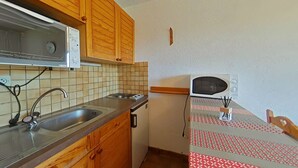 Eine kompakte Küche mit Holzausstattung, einem Edelstahlspülbecken, einer Mikrowelle und einem kleinen Kühlschrank.