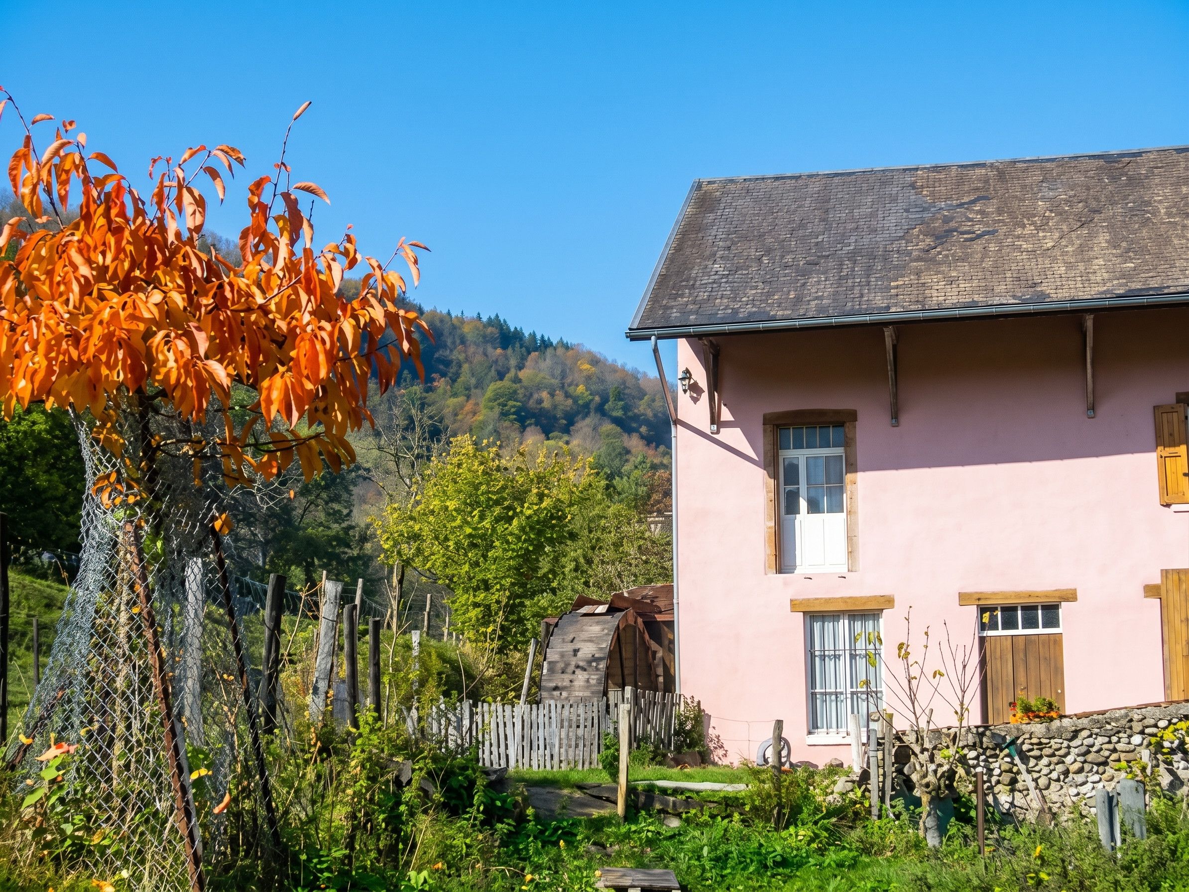 Un bâtiment rose avec un toit en pente, une clôture en bois et un mur de pierre.