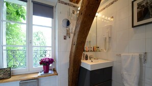 A bathroom with a large window, a wooden beam, a sink, and a mirror. - C3DD Strolling (París)
